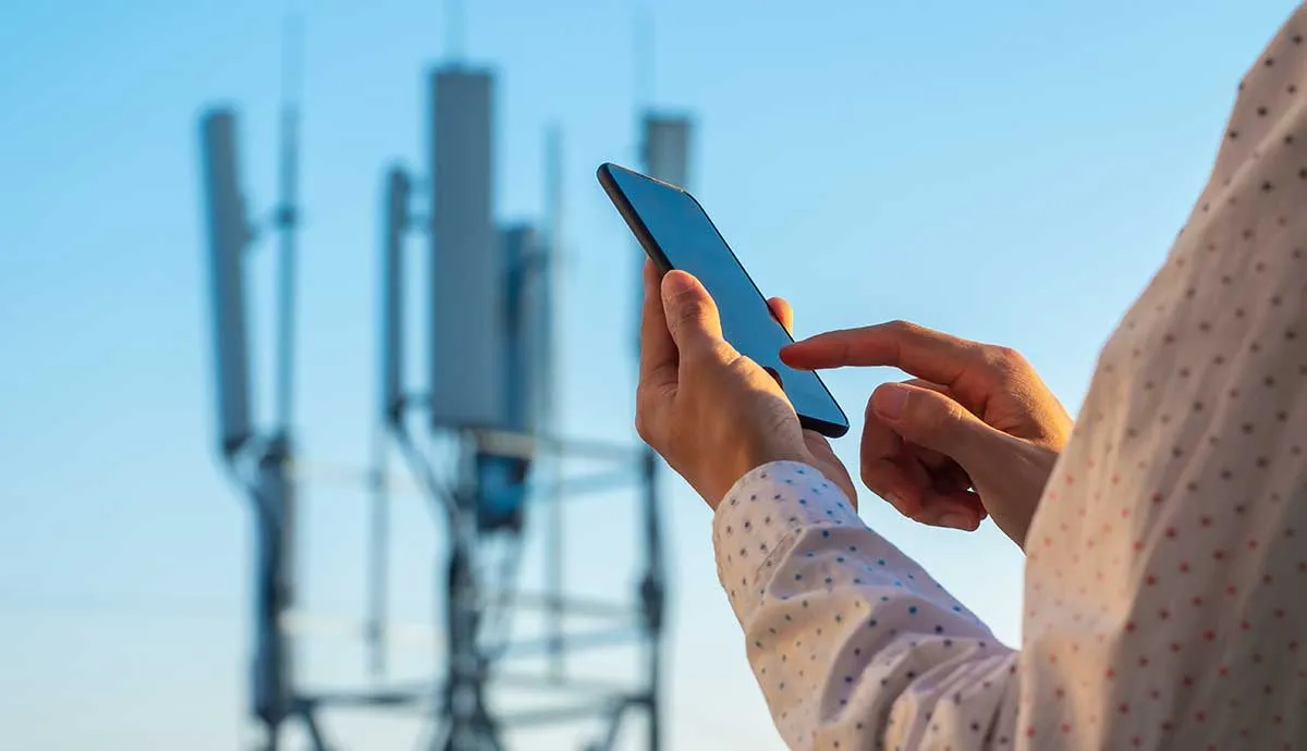 Person holding cell phone with cell towers in background