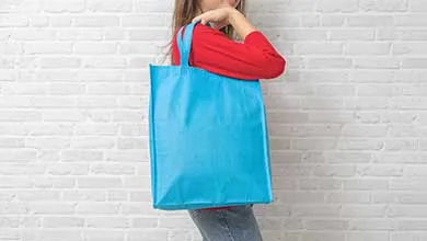 Woman in red shirt with a blue tote bag against a white brick wall